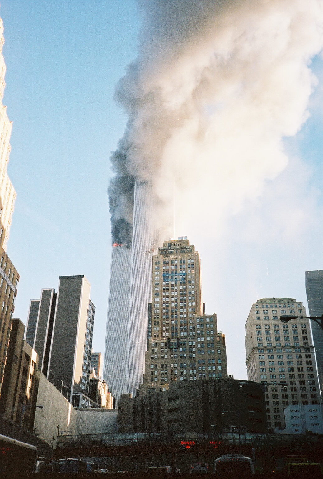 The first frame taken after getting off the bus. Standing on the plaza of the Brooklyn Battery Tunnel facing north; the South Tower struck within the last two minutes, white dust and smoke flowing from holes on both sides.